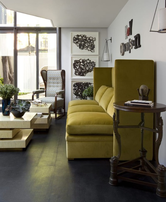 Modern living room with green sofa, artistic wall art, wooden coffee table, and a large window providing natural light.