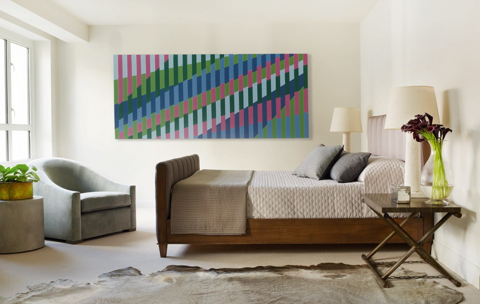 Modern bedroom with wooden bed, abstract art on the wall, a side table with lamp, and a window letting in natural light.