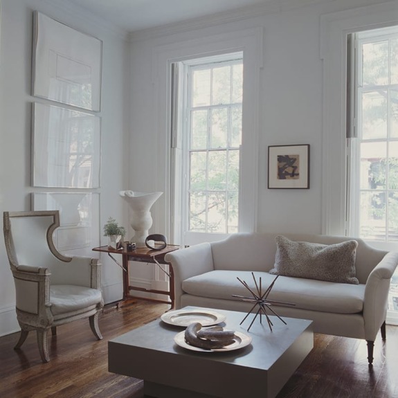 A modern living room with a white sofa, an elegant armchair, large windows, and minimalist decor.
