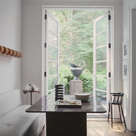 Dining area with a wooden table, open French doors leading to a garden with a swan statue.