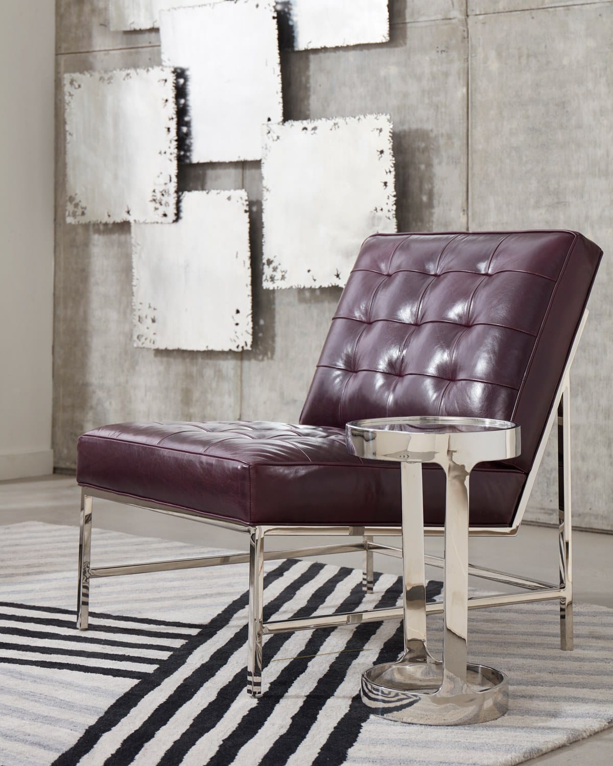 Modern leather chair with metal frame next to a sleek side table, set against an industrial-style backdrop with decorative art.