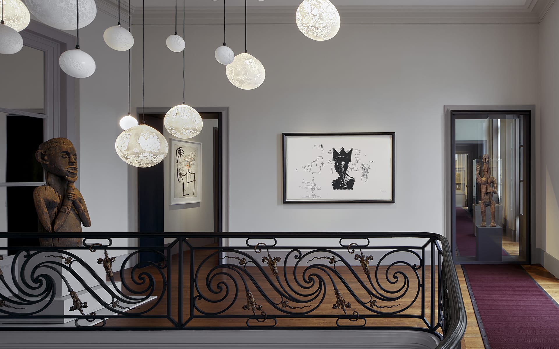 Art gallery interior with sculpture, framed artwork, ornate railing, and modern pendant lights.