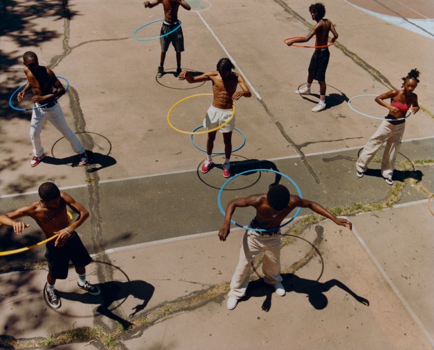 Group of people hula hooping on a sunny day on an outdoor basketball court.
