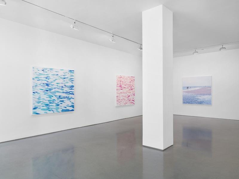 Art gallery interior with abstract water-themed paintings on white walls, and a central pillar in a spacious room.