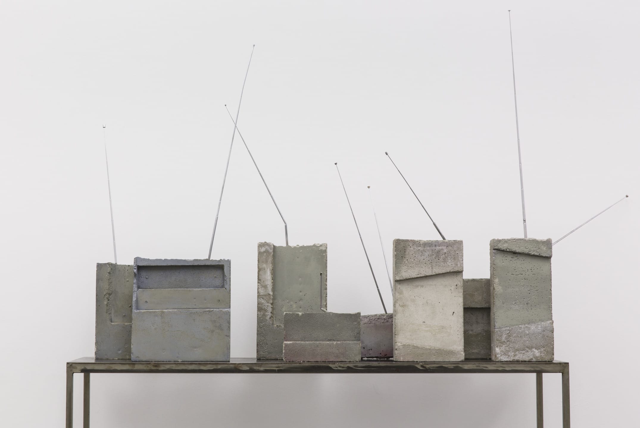 Abstract sculpture of six geometric concrete blocks with metal rods on a metal table against a plain white background.