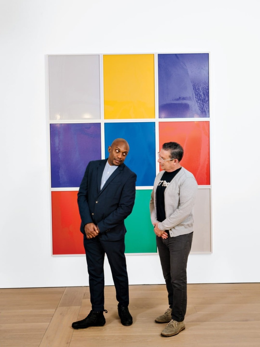 Two individuals standing in front of a colorful, modern art piece with nine squares in a grid layout, engaging in conversation.