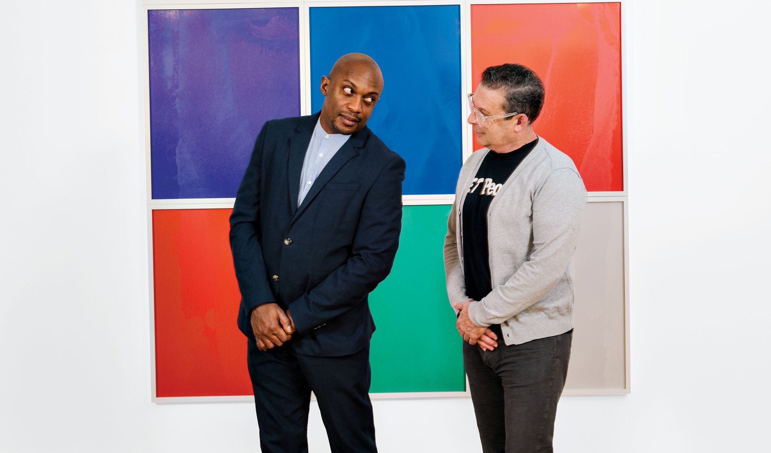 Two people standing in front of a colorful abstract art piece, one in a suit and the other in casual attire.