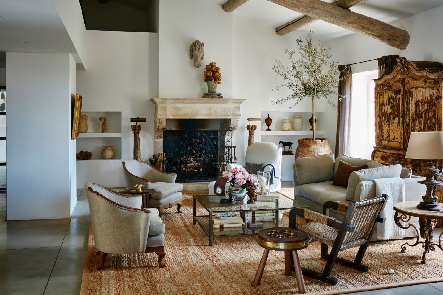 Cozy rustic living room with fireplace, comfortable seating, decorative plants, wooden ceiling beams, and natural light.