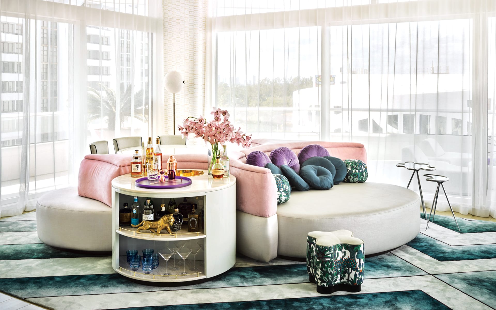 luxurious modern living room with a round sectional sofa, vibrant cushions, a swivel minibar, and large windows with sheer curtains