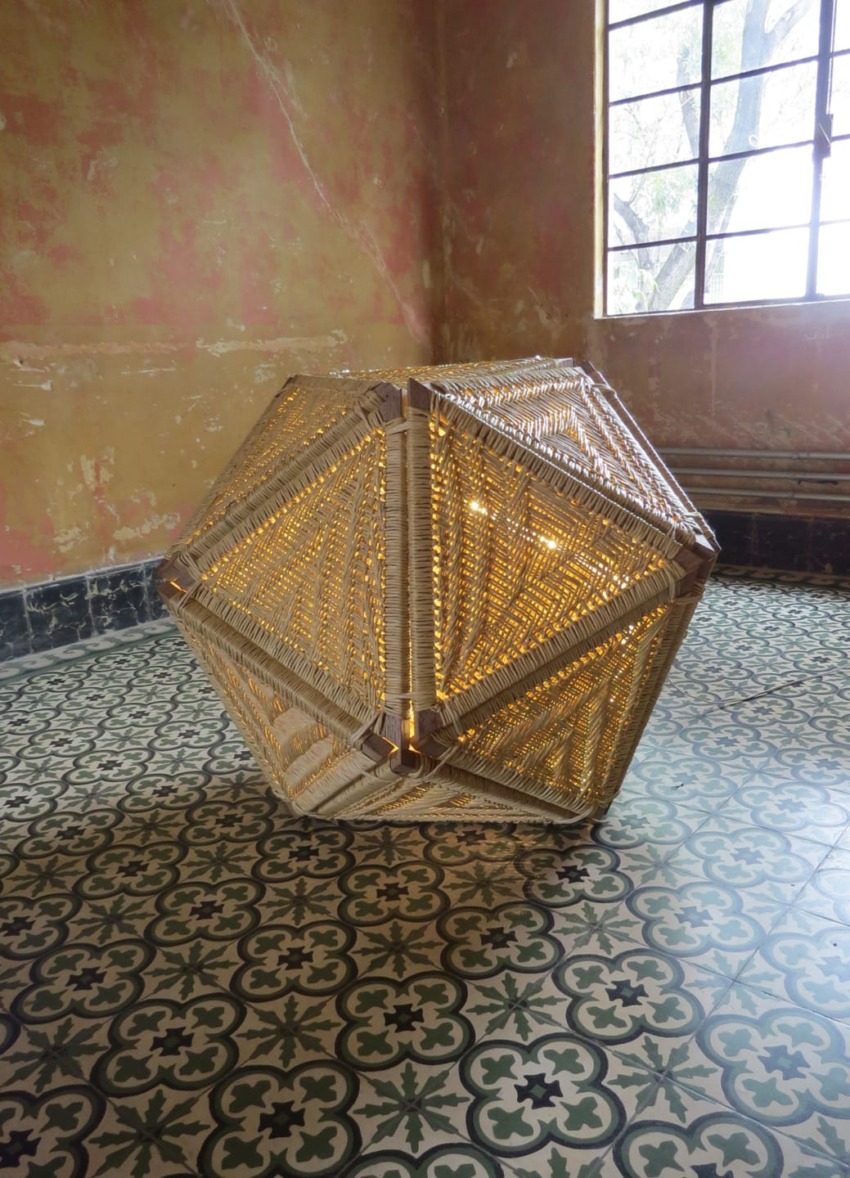 Geometric woven lamp with warm light on patterned tile floor in vintage room with large window.