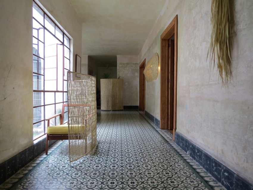 Hallway with patterned tile floor, wicker room divider, wooden doors, and a large window letting in natural light.