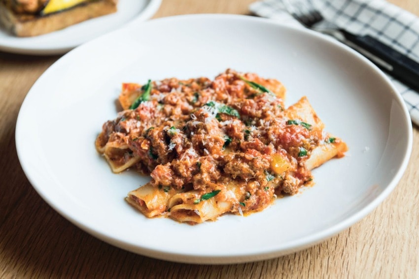 Plate of pasta with meat sauce garnished with fresh herbs on a wooden table.