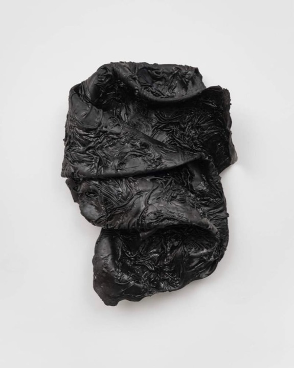 Abstract black textured sculpture on a light background, featuring intricate folds and patterns resembling fabric.