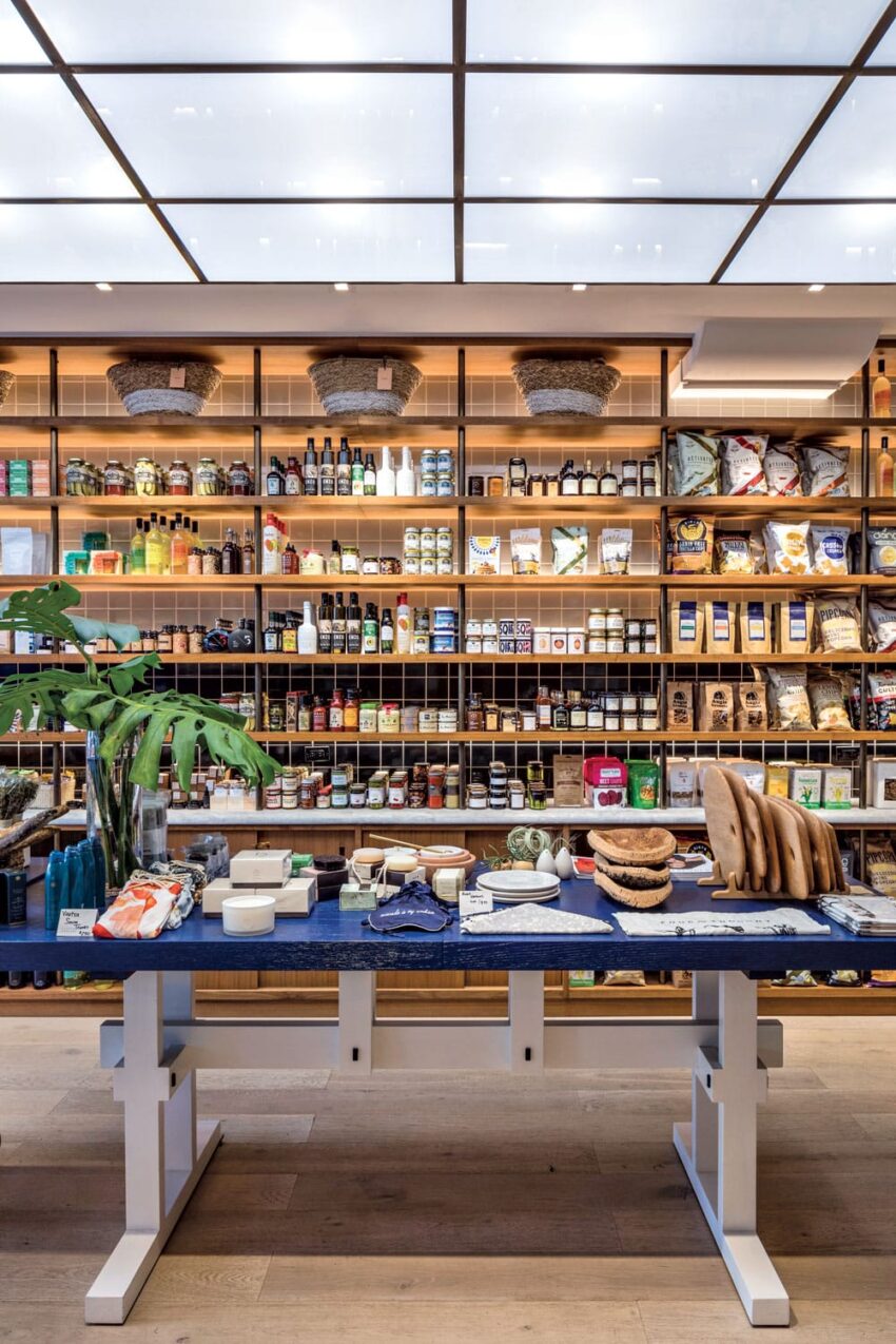 Gourmet grocery store interior with shelves of food products and a central table displaying various items.