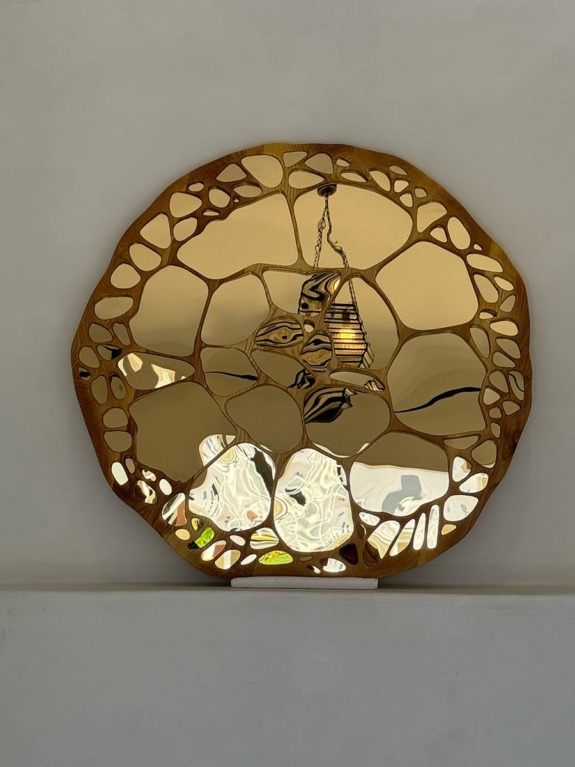 Artistic round mirror with abstract patterns and central lamp reflection on a plain wall background.