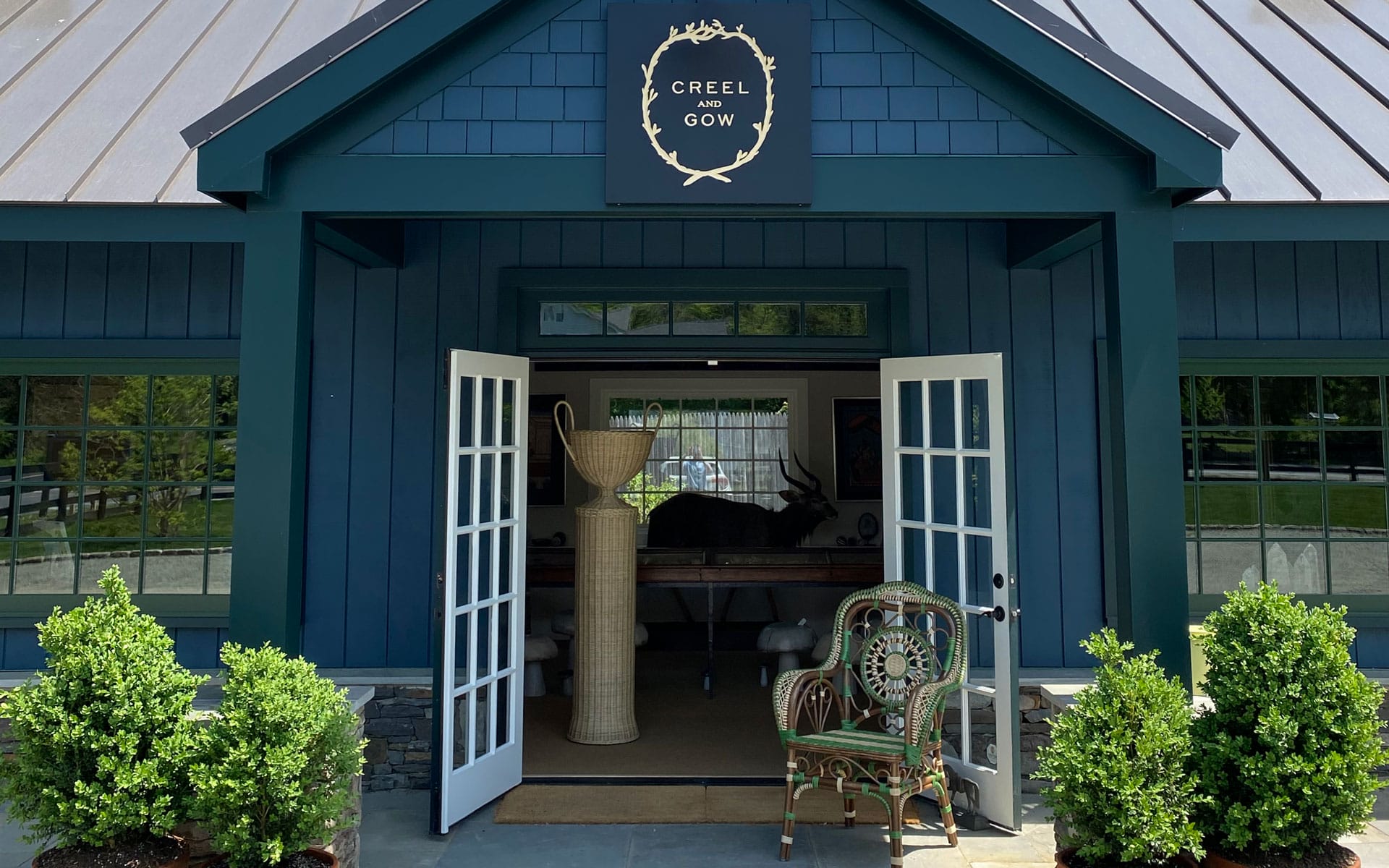 Storefront with open double doors, a chair in front, and plants on each side. Sign above the door reads "Creel and Gow".