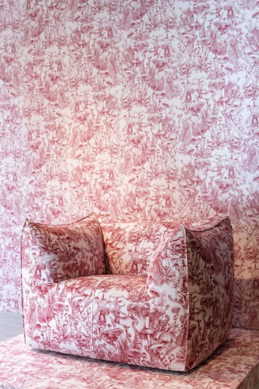 Patterned red and white armchair blending seamlessly with matching wallpaper background.