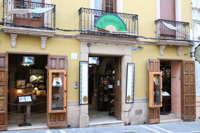 Exterior of a charming art and craft shop with open wooden doors and colorful displays inside on a sunny street.