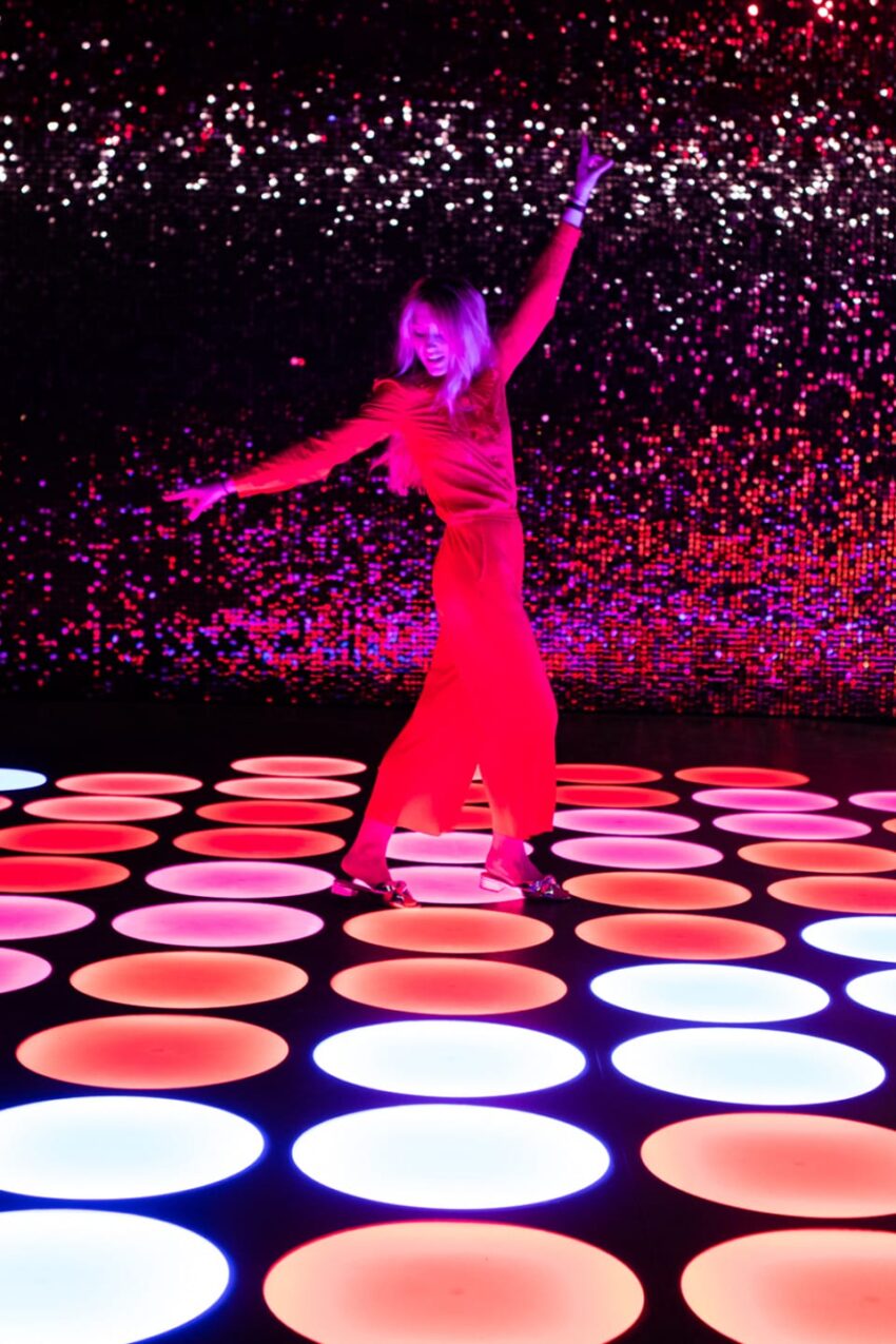 Person dancing on a colorful LED dance floor with illuminated circles and a vibrant pink and purple background.