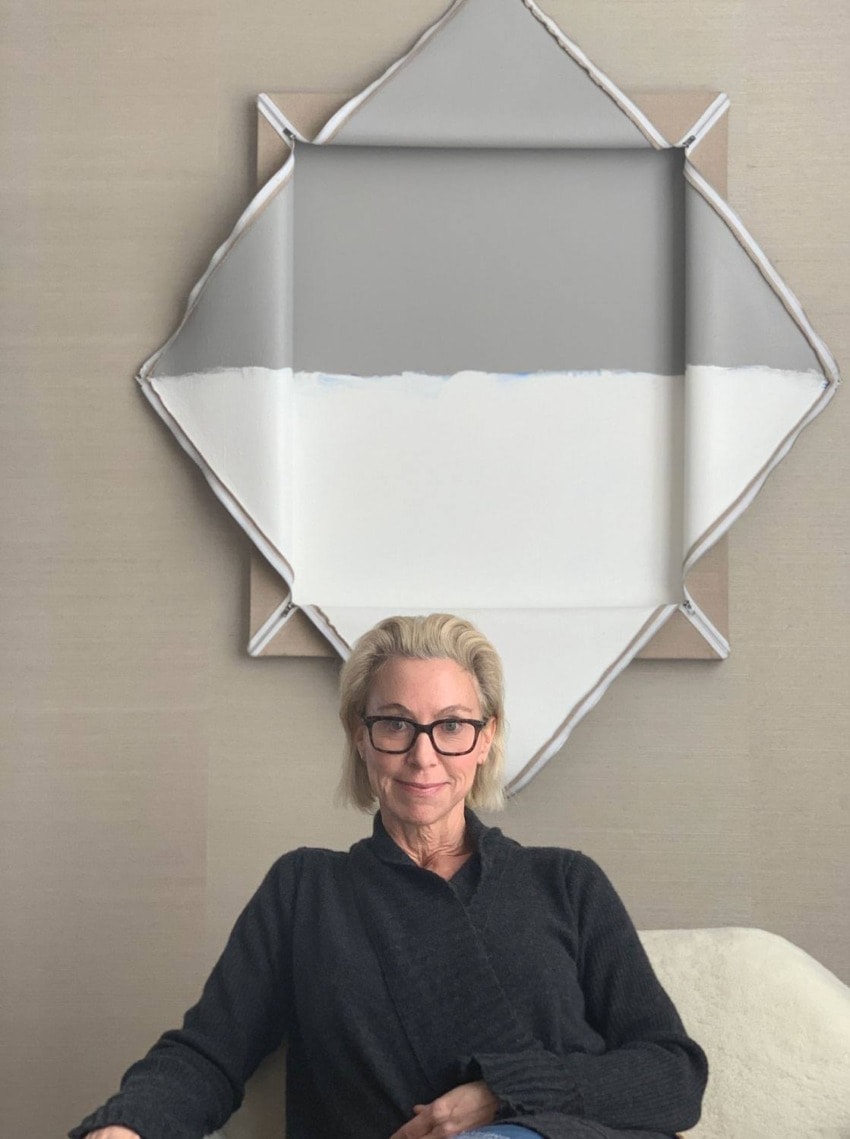 Person sitting in front of abstract artwork with geometric design on a beige wall background.