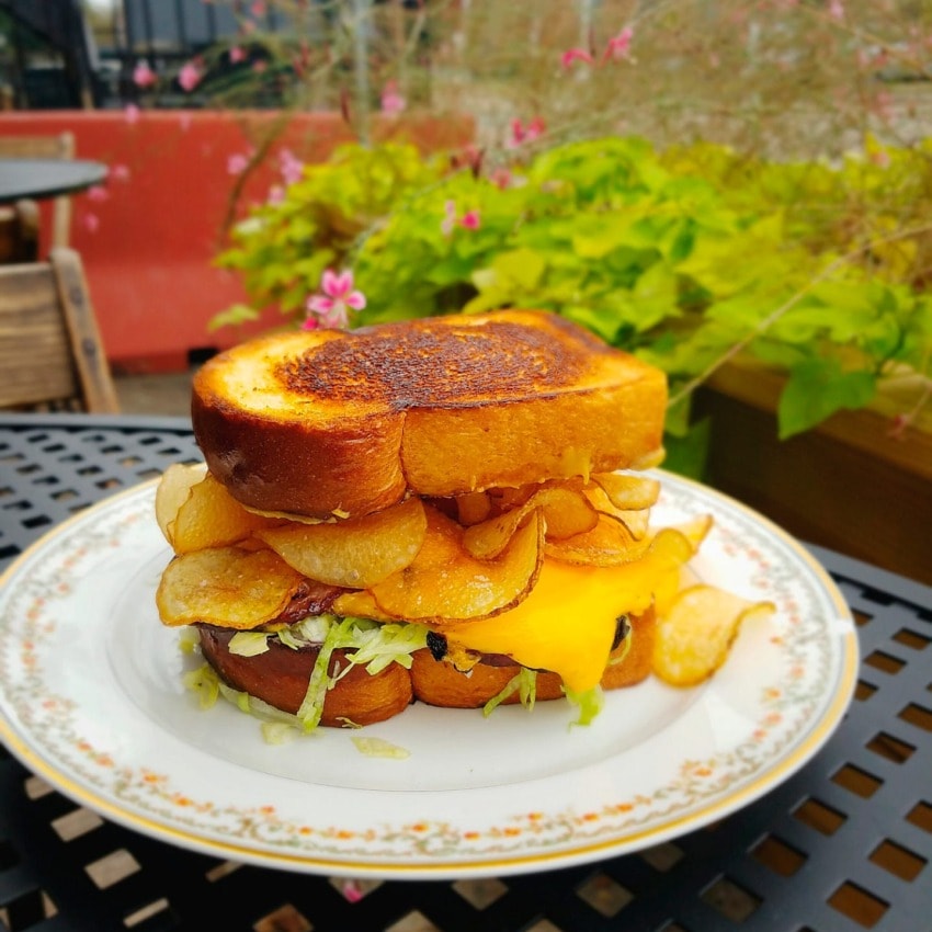 Grilled cheese sandwich with potato chips and lettuce on a decorative plate, outdoors on a metal table.