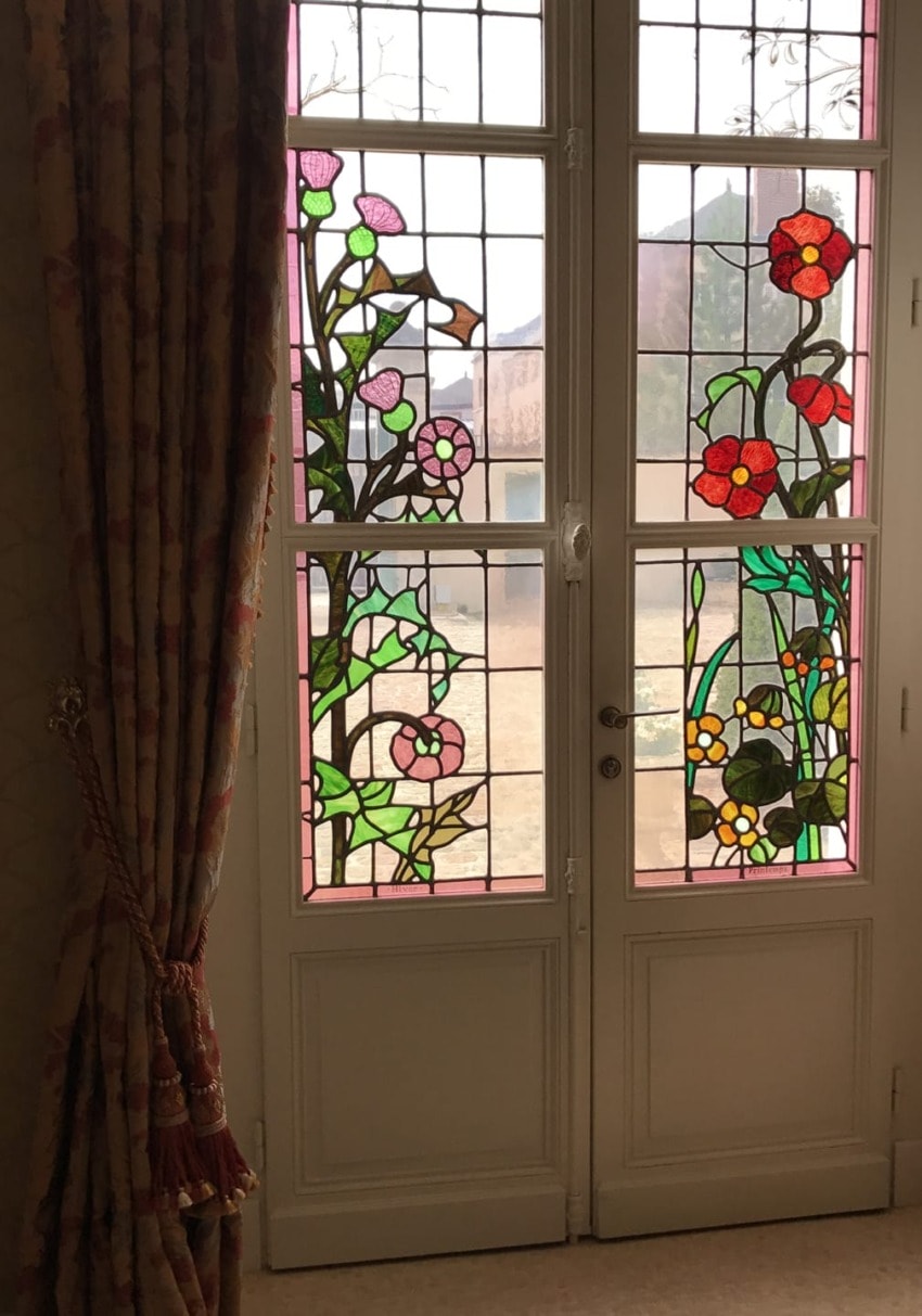 Stained glass doors with floral patterns in a dimly lit room with curtains on the side.