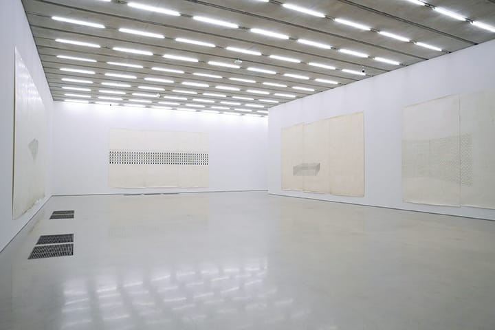 Minimalist art gallery with large abstract canvases on white walls under a ceiling with rows of fluorescent lights.