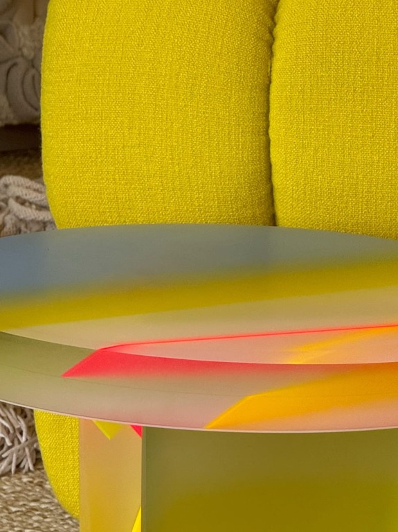 Modern yellow chair and unique glass table with colorful reflections in a cozy living space.