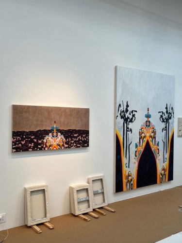 Paintings on a gallery wall with abstract designs, two smaller framed canvases leaning below.