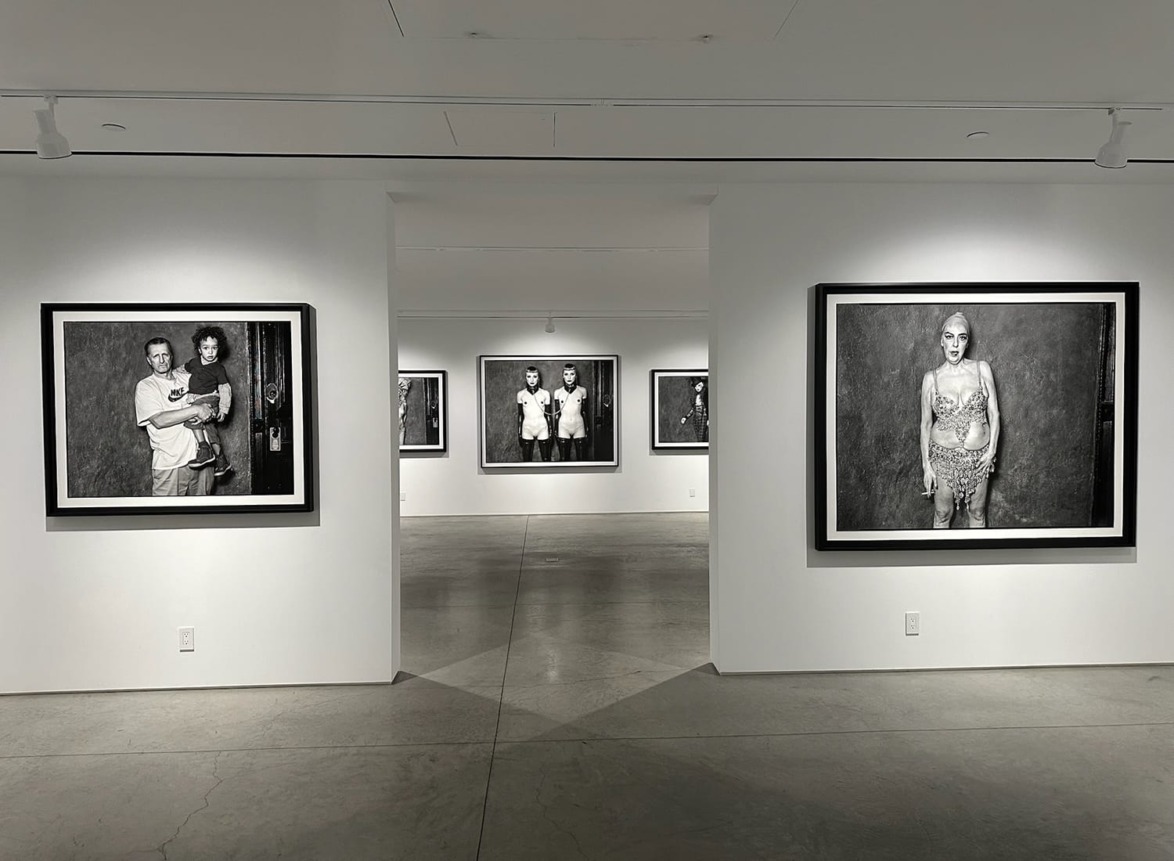 Art gallery with black and white portraits on walls, showcasing various individuals in a modern, minimalistic space.