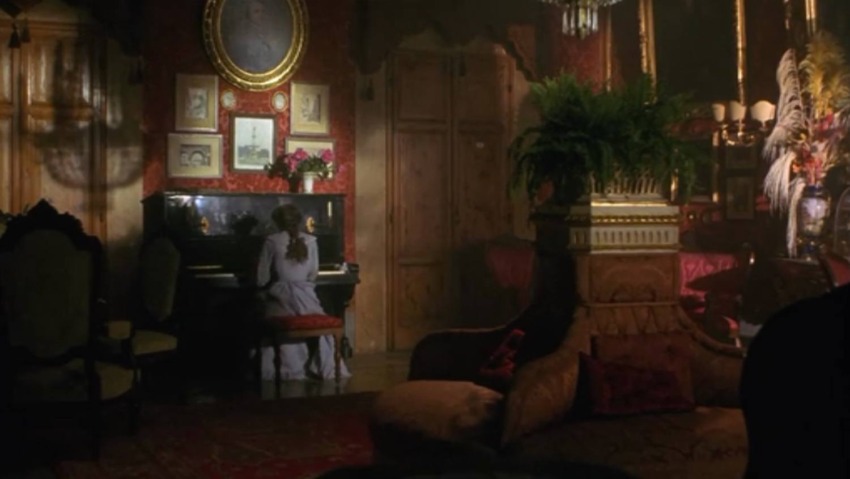 Woman playing piano in an ornate room with red walls, gold accents, and vintage decor.