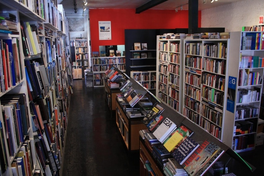 Bookstore interior with shelves filled with novels and non-fiction books, featuring a red accent wall and wooden floor.