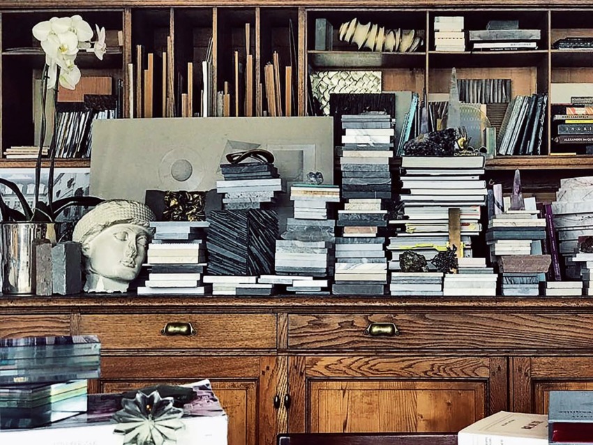 Wooden shelves filled with stacked books, art pieces, and a potted orchid, with a bust sculpture among the items.