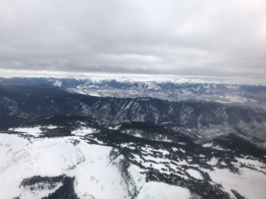 Snow-covered mountains and valleys under a cloudy sky, with rugged terrain and patches of forest visible.