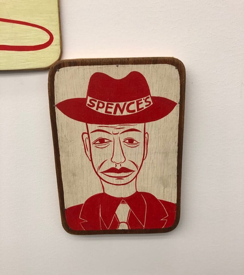 Vintage-style artwork of a man in a hat with "Spence's" text, red and beige colors, displayed on a wall.
