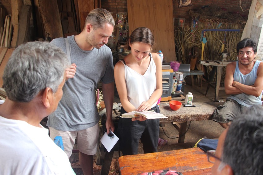 Group of people in a workshop discussing a book, surrounded by woodworking materials and tools.