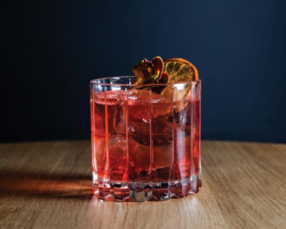 A glass of Negroni cocktail with ice and an orange slice garnish on a wooden table.