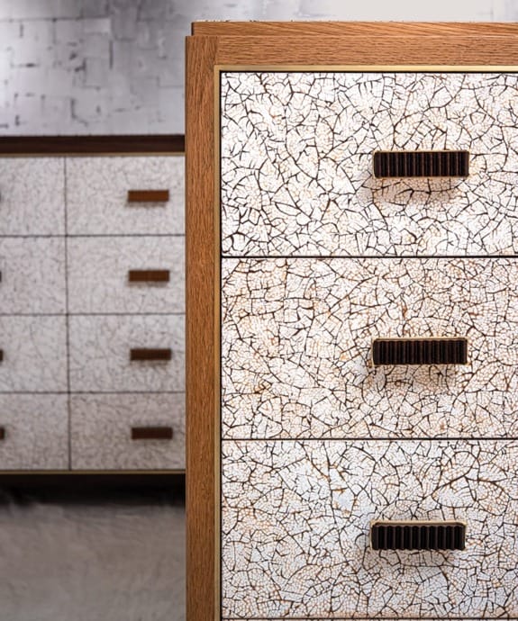 Close-up of a wooden dresser with three drawers featuring a white cracked paint design and dark handles.
