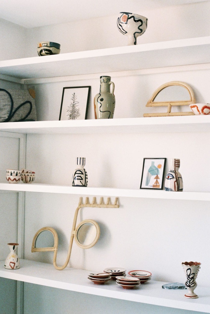 Shelves displaying various ceramic vases, abstract sculptures, framed art pieces, and patterned bowls in a minimalist style.