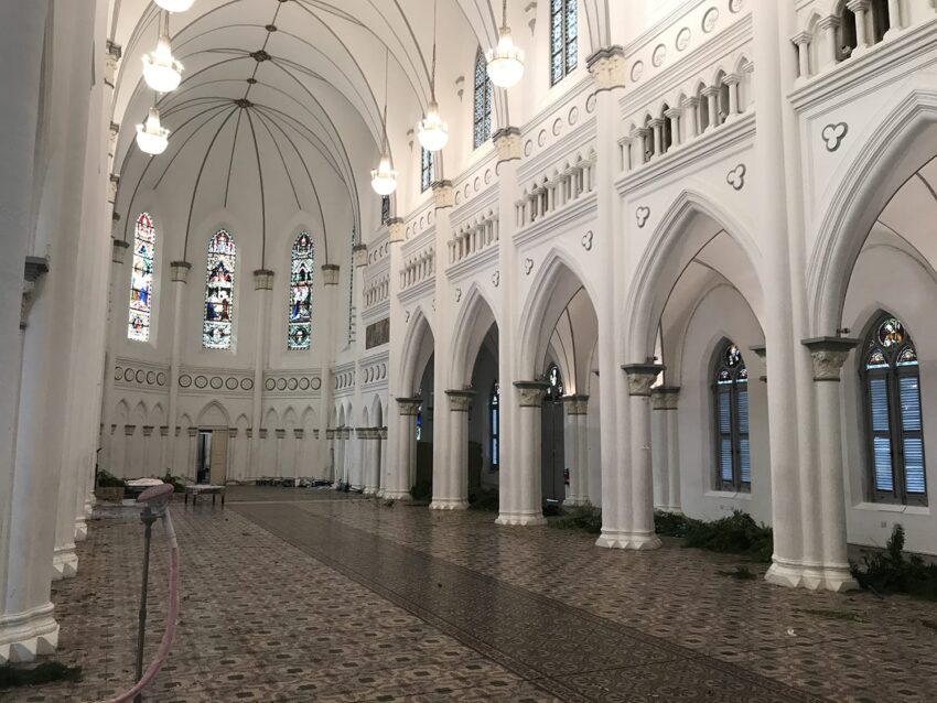 Interior of a historic white cathedral with stained glass windows, ornate arches, and patterned floor tiles.