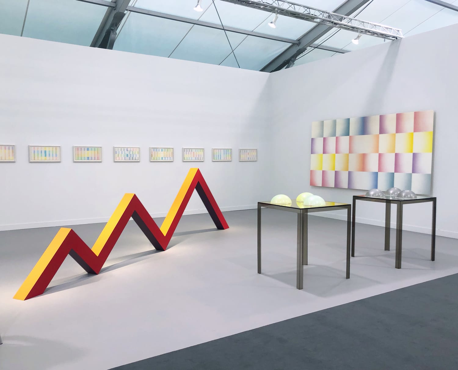 Modern art gallery with geometric sculptures, colorful wall art, and minimalistic tables displaying spherical objects.