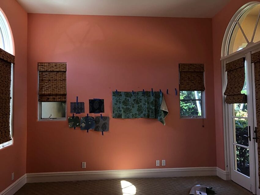sunlit room with coral walls, arched windows, bamboo shades, and fabric swatches pinned to the wall for decoration