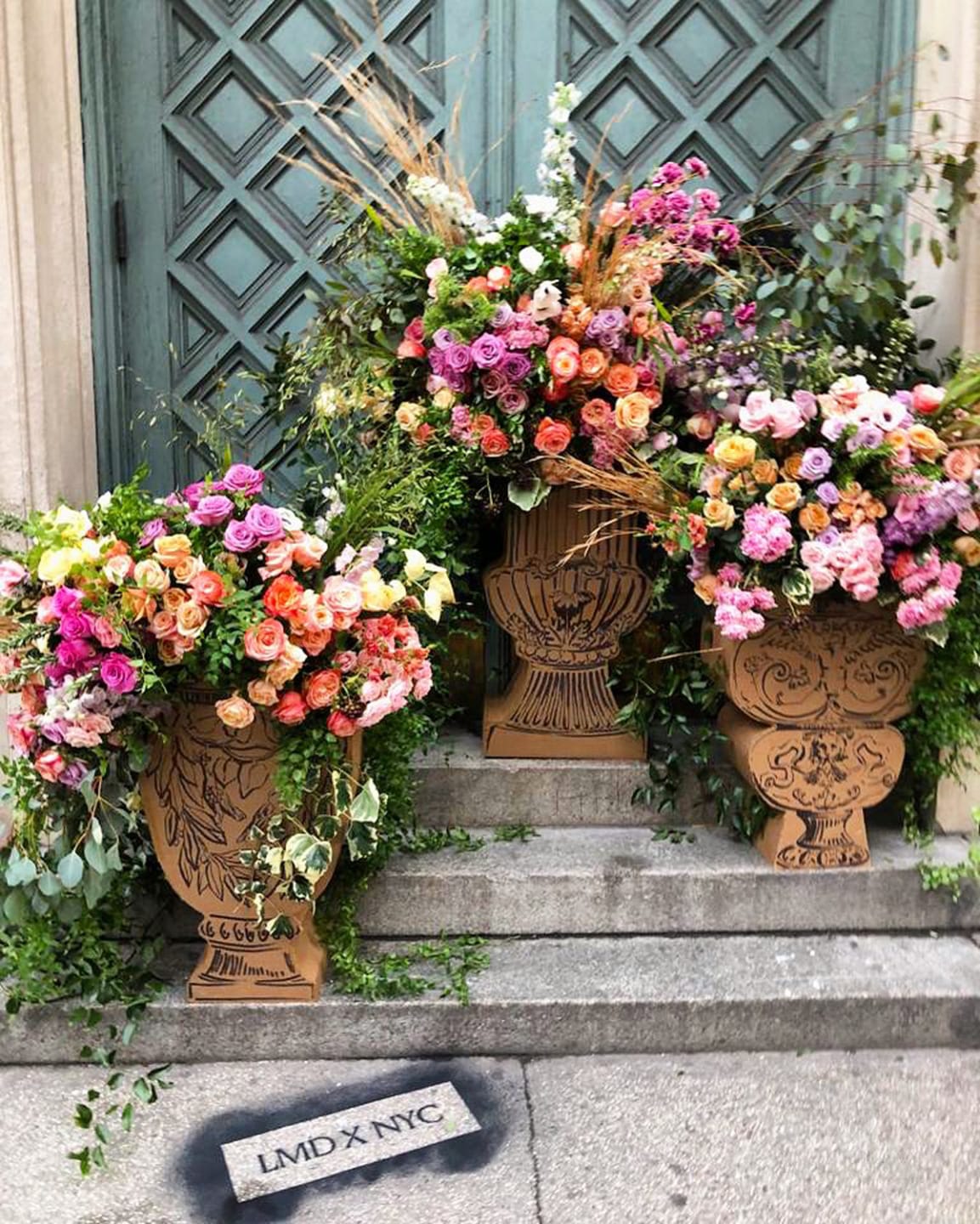 Beautifully arranged colorful flower bouquets in ornate vases on stone steps near a decorative door.