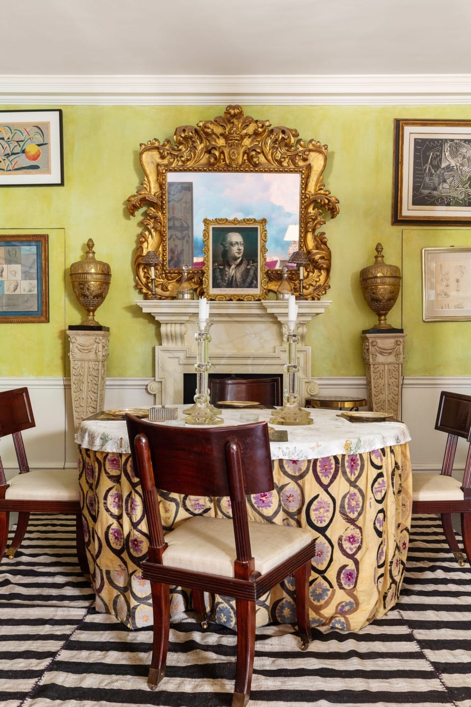 Eclectic dining room with ornate gold mirror, framed art, round table, upholstered chairs, and decorative vases.