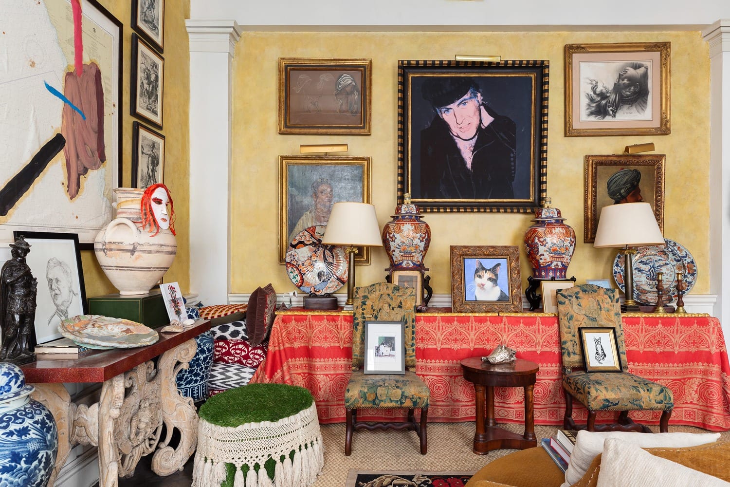 Eclectic living room with various framed art pieces, patterned textiles, and vintage vases displayed on a decorated mantel.