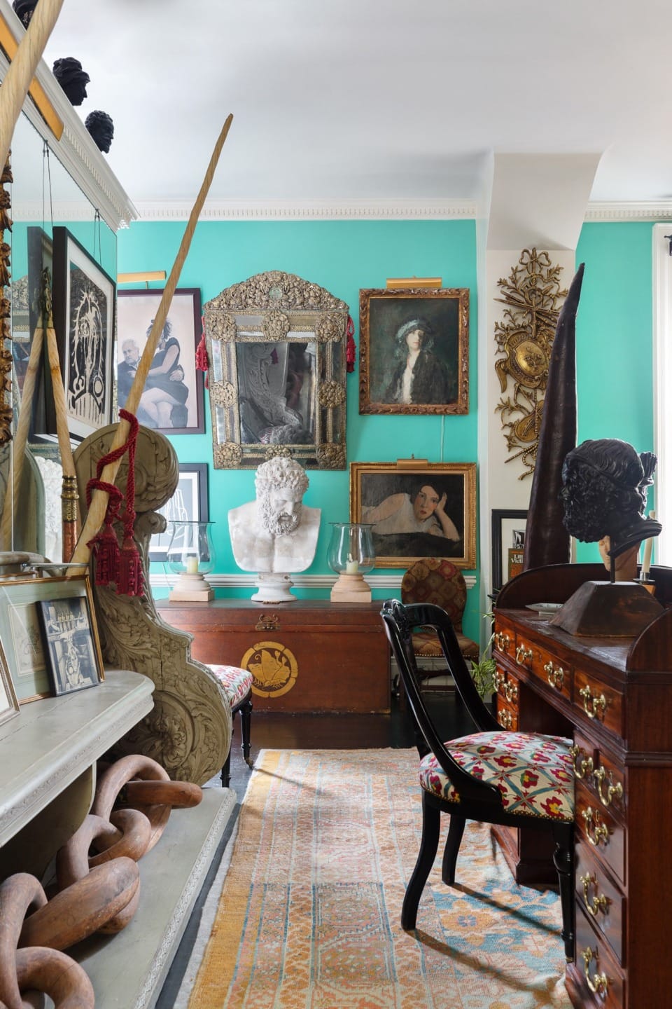 Eclectic room with turquoise walls, diverse artworks, sculptures, ornate furniture, and a decorative rug.