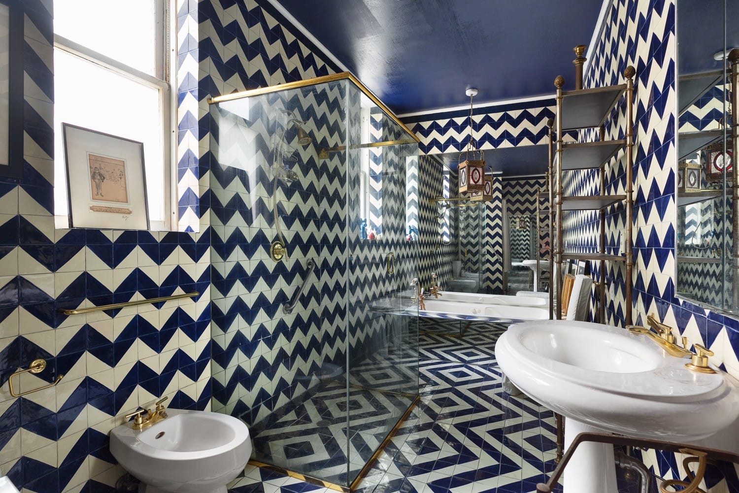 Bathroom with blue and white geometric tiles, glass shower enclosure, white sink, and bidet.