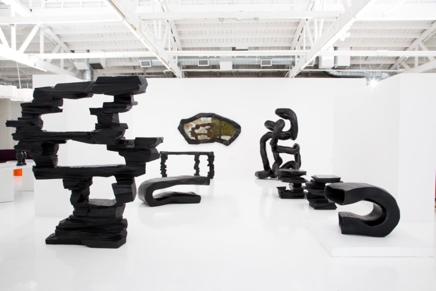 Contemporary art gallery with abstract black sculptures displayed on a white floor and walls.