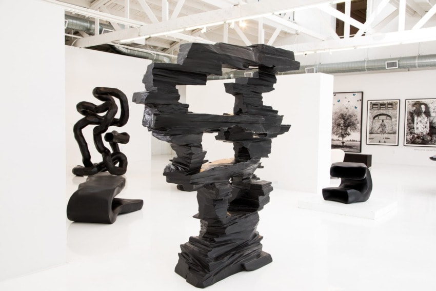 Modern art gallery with abstract black sculptures and framed artwork on white walls, featuring bright and open space.