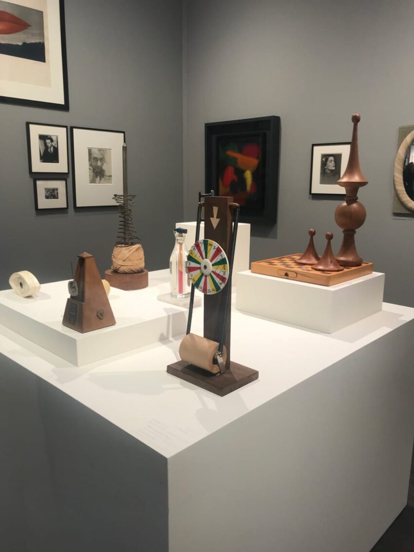 Museum exhibit with various abstract sculptures and framed artworks on a gray wall.